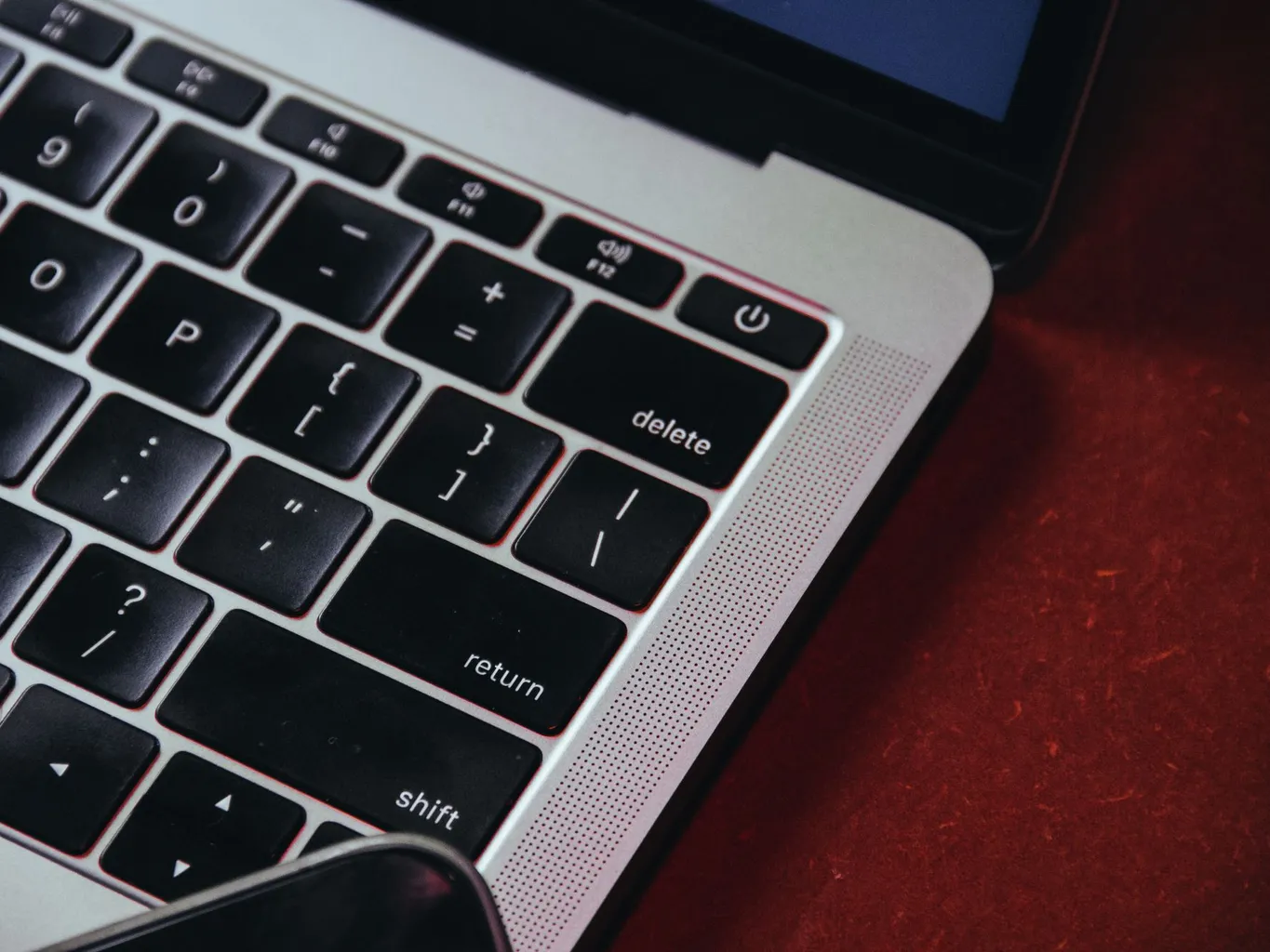 A laptop keyboard on a warm red desk with the Delete key in sharp focus