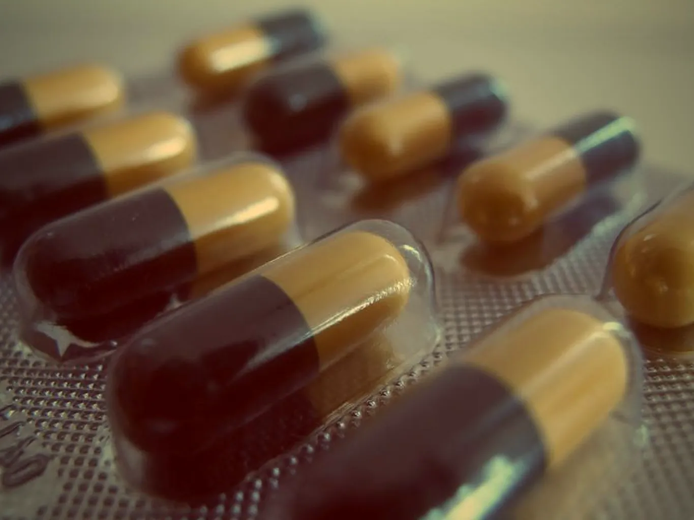 Close-up of two-tone medication capsules sealed in a foil blister pack under warm amber light