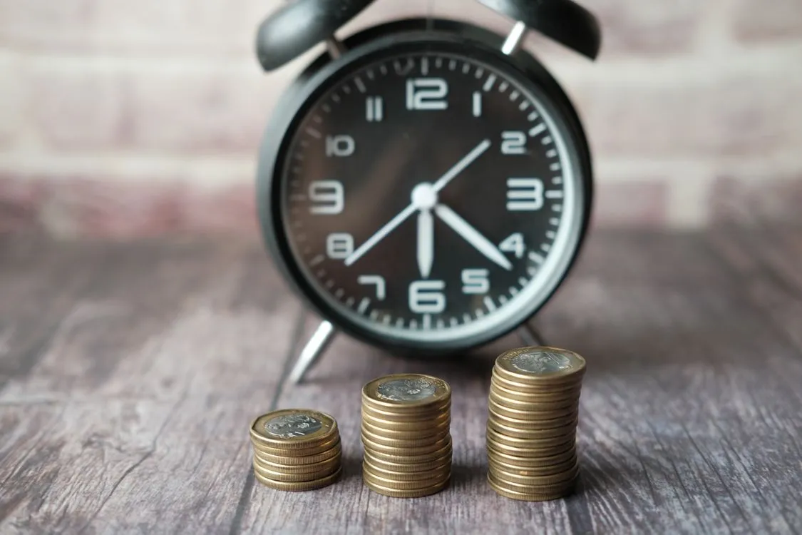 Stacked coins next to a classic alarm clock on a desk